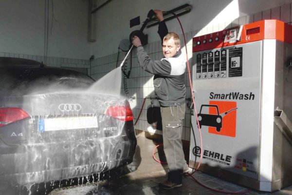 Ein mann wäscht sein auto mit schaum in einer  selbstbedienungsautowaschanlage mit rädern und reifen in der nähe